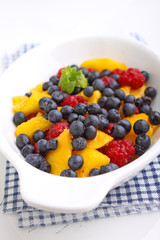 fresh berries in a white plate on a white background: raspberries, blueberries, peach.