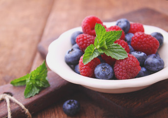 healthy breakfast. raspberries and blueberries in a white bowl on a wooden background.