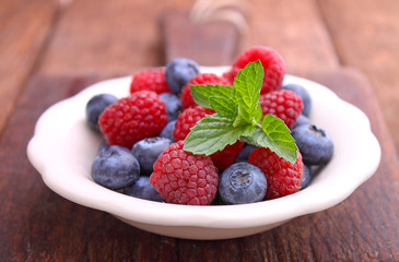 healthy breakfast. raspberries and blueberries in a white bowl on a wooden background.