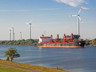 Containerschiff auf einem Fluss zwischen zwei Windkraftanlagen