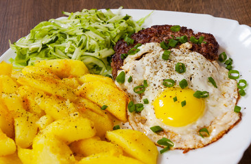 Grilled Beef Steak with fried egg, vegetables salad and potato in a white plate on wooden table