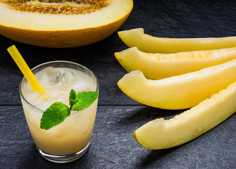 slices of melon juice from the melon with mint leaves and a half melon on the black table