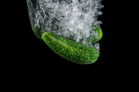 Two fresh cucumbers with water splash isolated on black background.