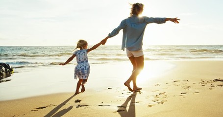 Mother and daughter having fun walking and playing on the beach at sunset