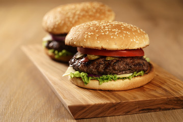 two homemade burgers on olive board on oak table