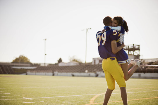 Football player picking up cheerleader in a lover's embrace.