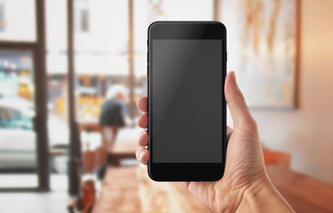 Smart phone in man hand. Coffee shop in background. Blank screen for mockup.