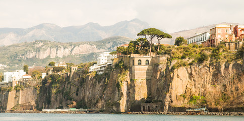 A sunlit cliff over Sorrento with trees and houses on top of it.