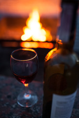 bottle and glass of red wine with fire on background;