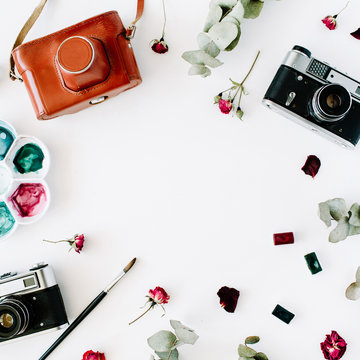 Flat lay. Artist workspace frame with vintage retro photo camera, and watercolor, red roses and eucalyptus. Top view arrangement