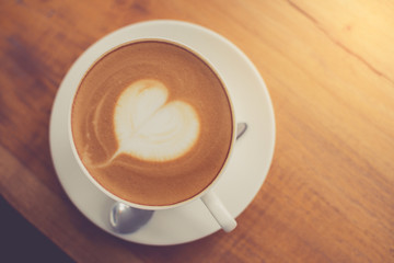 A cup of coffee with heart pattern in a white cup on wooden background made with retro filter.
