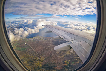 View from airplane window on green fields ,  clouds and sea