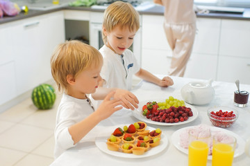 Obraz na płótnie Canvas Two boys preparing breakfast in white kitchen