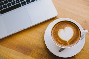 A cup of coffee with heart pattern in a white cup on wooden background