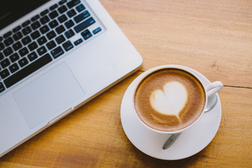 A cup of coffee with heart pattern in a white cup on wooden background