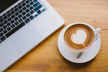 A cup of coffee with heart pattern in a white cup on wooden background