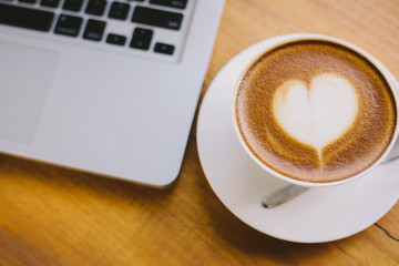 A cup of coffee with heart pattern in a white cup on wooden background