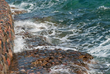 Photo of beautiful clear turquoise sea ocean water surface with ripples and bright splash on stone seascape background, horizontal picture