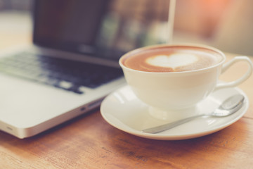Laptop and coffee cup on wooden table with vintage filter