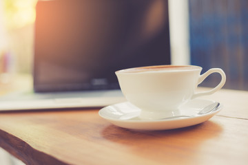 Laptop and coffee cup on wooden table with vintage filter