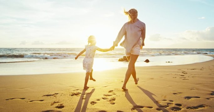 Mother and daughter having fun walking and playing on the beach at sunset
