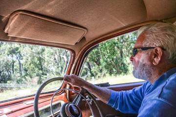 Interior view of 1940’s restored vintage car being driven by elderly man with grey hair and beard wearing sunglasses.