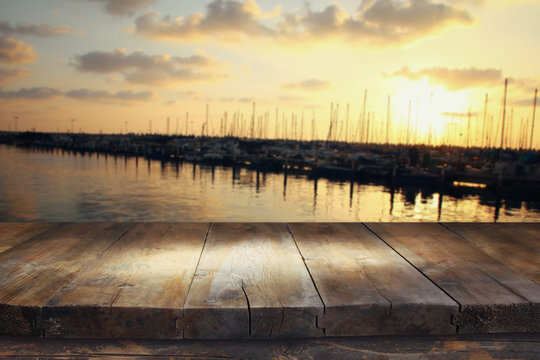 wooden table in front of blurred yachts in pier at sunset