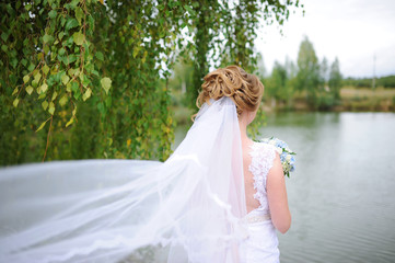 Fototapeta na wymiar Beautiful young bride on the bank of the river in foliar summer forest