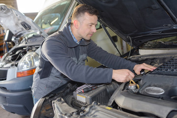Plakat mechanic using laptop while repairing car in garage
