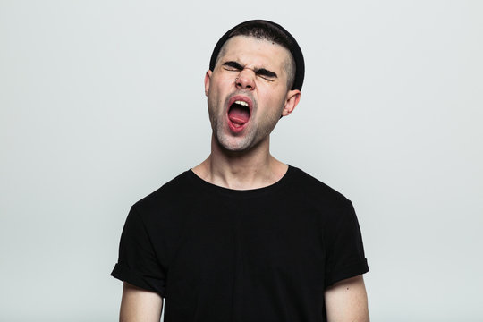 Studio portrait of handsome man in black yawning on the white background.