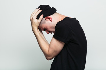 Side view of young man in stress pose on white background with hands on head. Studio shot.