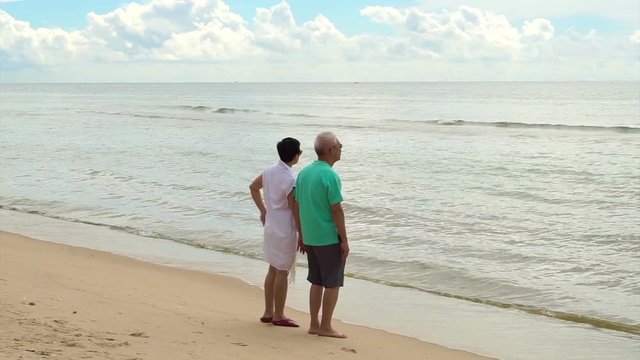 Asian senior couple walking happily by the beach. holding hand and talk with each other