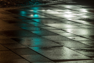 leuchtende Steinplatten im Regen bei Nacht mit Spiegelung von Ampellicht und Autoschenwwerfern