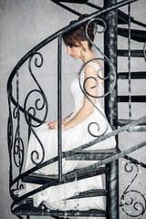 Beautiful young bride sitiing on a forged stairs in a bright interior