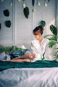 Beautiful young bride sitting on a bed covered with a green blanket in a room with flowers