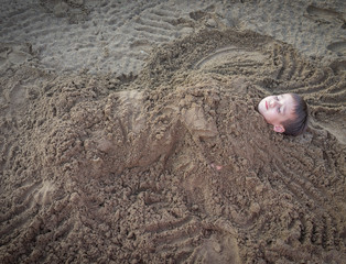 Cute kid burried in the sand for fun