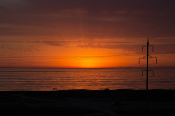 Fototapeta na wymiar Power lines near the sea in a background of red sunrise light