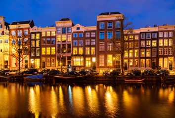 Naklejka premium Typical dutch houses over canal with reflections illuminated at night, Amsterdam, Netherlands