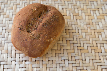 Loaf of home-baked rye bread with herbs. One whole loaf of fresh bread lies on a wicker table. Straight off the ice bread.