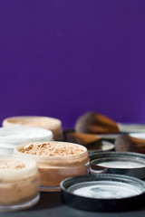 Vertical photo of make up mineral powder of beige and white colors and make up brushes on purple background
