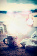 Snowflakes Mug with hot beverage , knitting mittens and bokeh  on frost window sill at winter snow nature background