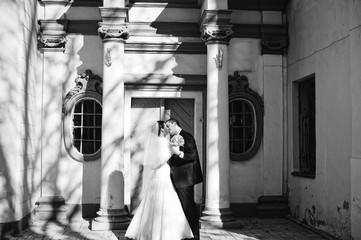 Fototapeta premium Gorgeous married couple kissing background old columns with shadow