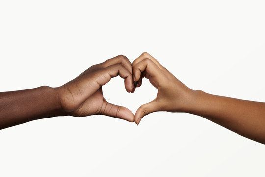 Two young dark-skinned people holding hands in shape of heart, symbolizing love, peace and unity. African man and woman showing heart-shaped hand gesture, expressing affection and togetherness