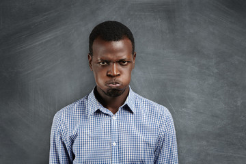 Portrait of irritated young dark-skinned teacher looking with grumpy and angry expression, blowing...