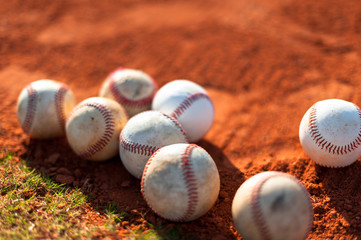 Several old well-worn little league baseballs on red infield dirt