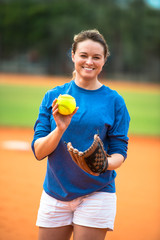 Smiling young woman softball player pitcher with bright fluorescent neon yellow ball in pitching...