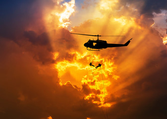    silhouette soldiers in action rappelling climb down from helicopter with military mission counter terrorism assault training on sunset background 