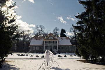 Bride walks to the old house across the frontyard full of snow