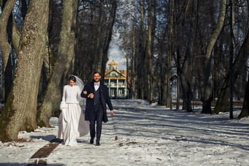 Smiling groom holds bride's hand walking with her along the snow