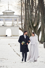 Stylish winter newlyweds walk along the snowed pass from the old